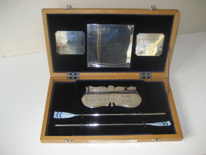 Two miniature silver sculling blades painted in Weybridge colours and lying in a velvet-lined presentation box with sliver plaques showing the names of winners